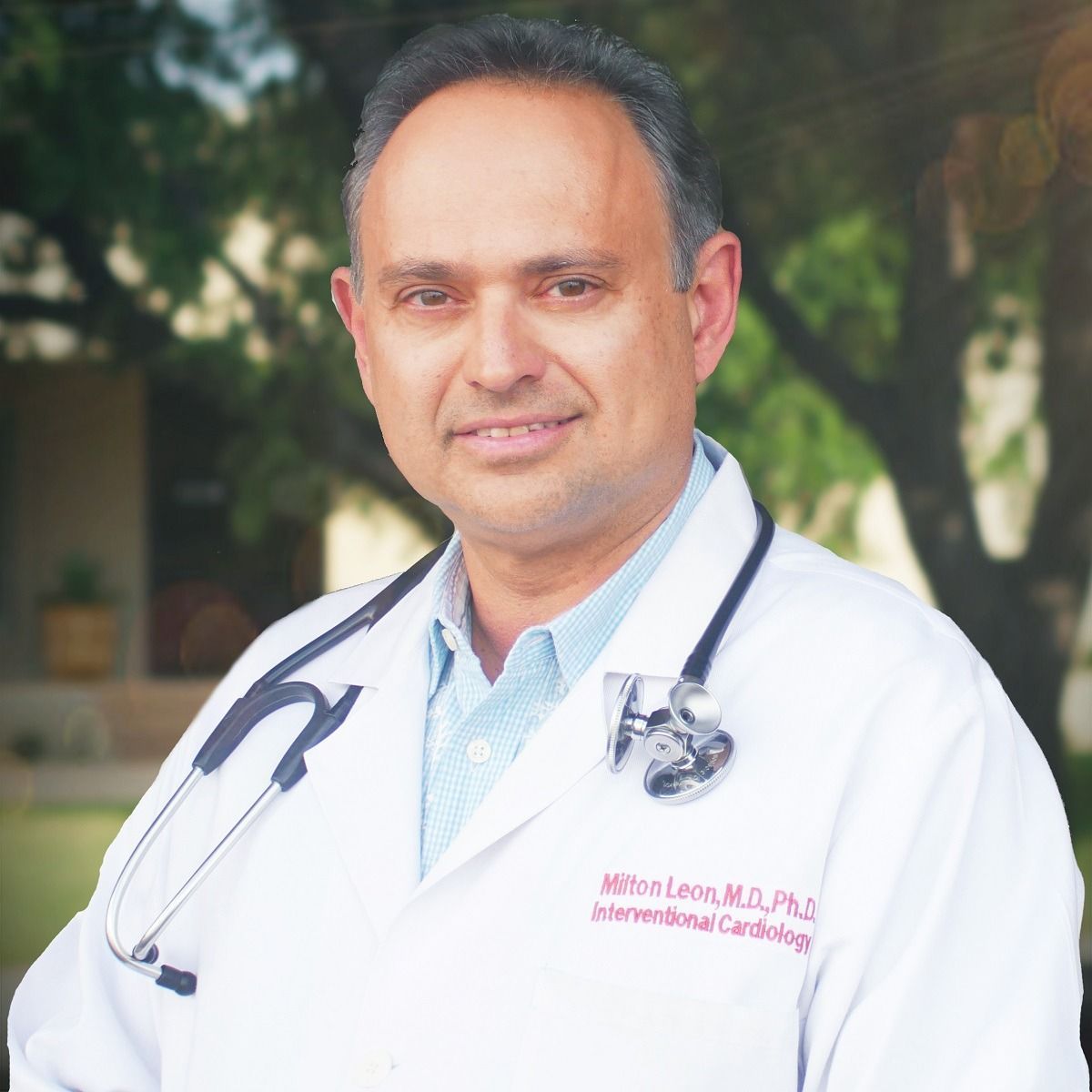 Portrait of a doctor in a white coat with stethoscope, standing outdoors against a blurred green background