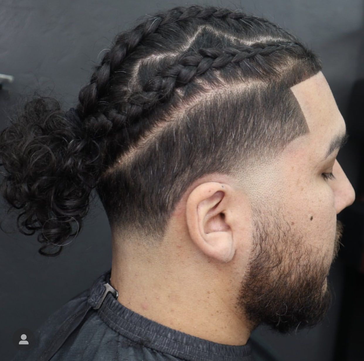 A man with a beard and braided hair showing his low-taper haircut style.