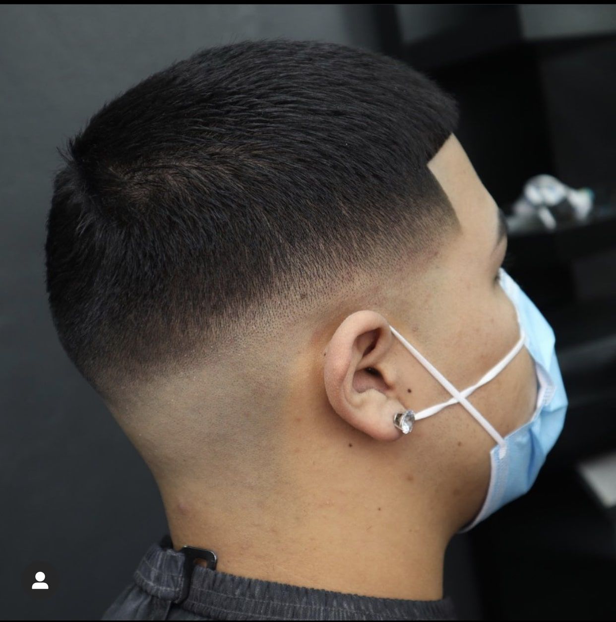 A man wearing a face mask and earrings showing his haircut style of a mid-fade.