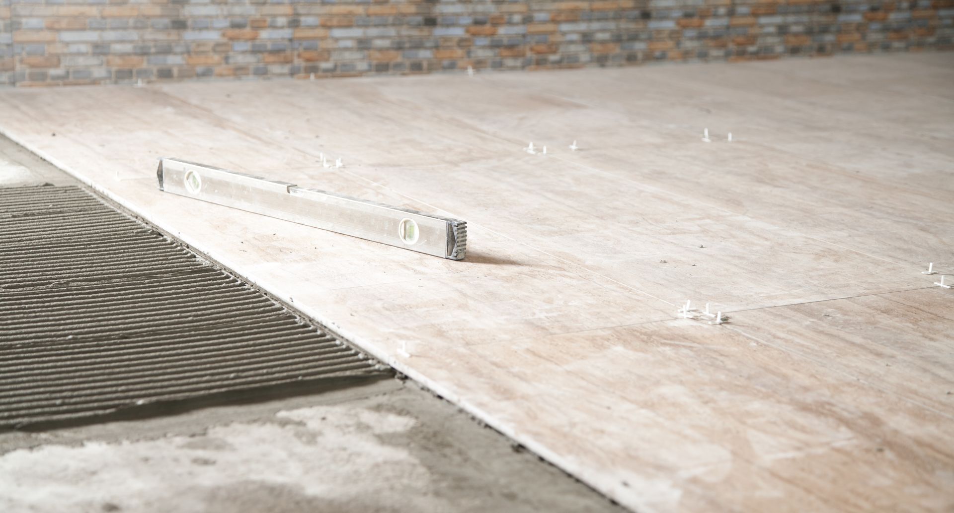 Floor tiling in progress with tiles, level, and spacers.