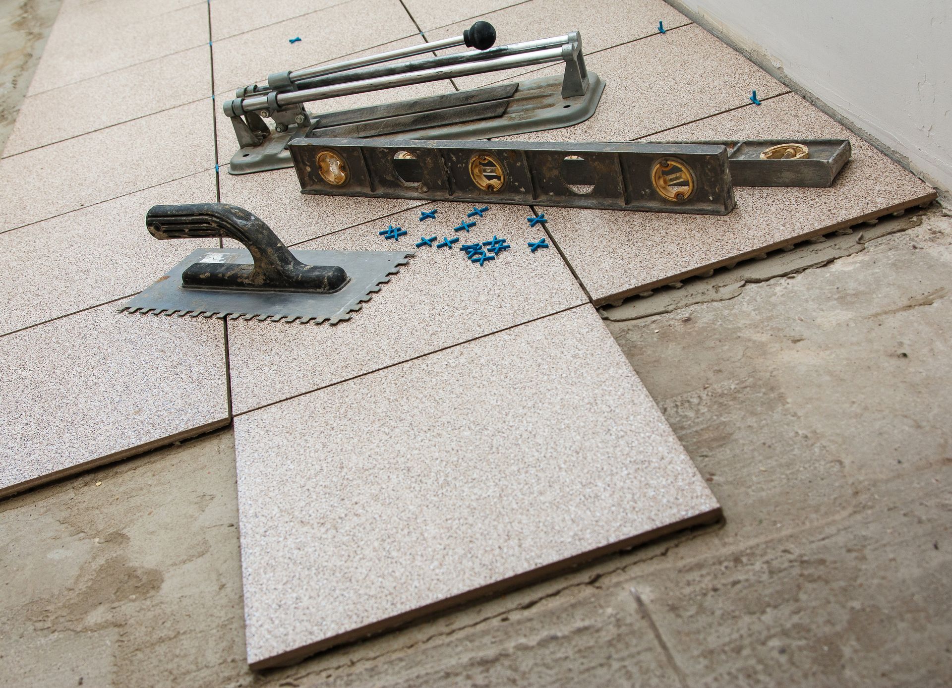 Tile installation tools: tile cutter, level, trowel, and tiles on a concrete surface.