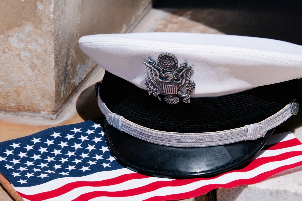US Navy officer's hat with emblem on an American flag, with a stone background.