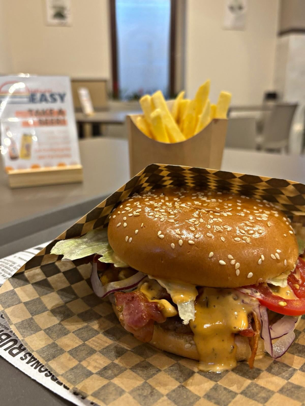 Hamburger al sesamo con formaggio fuso e patatine fritte su un vassoio, servito al bancone di un ristorante.