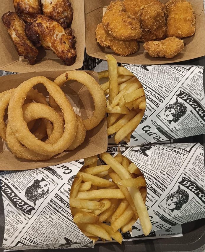 Assortimento di snack fritti: alette di pollo, anelli di cipolla, nuggets e patatine fritte in cestini foderati di carta.