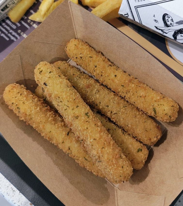 Quattro bastoncini di mozzarella impanati in una scatola da asporto su un tavolo.