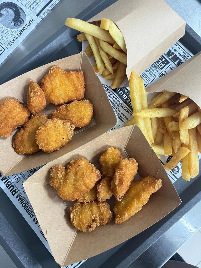 Su un tavolo ci sono scatole da asporto di crocchette di pollo e patatine fritte.