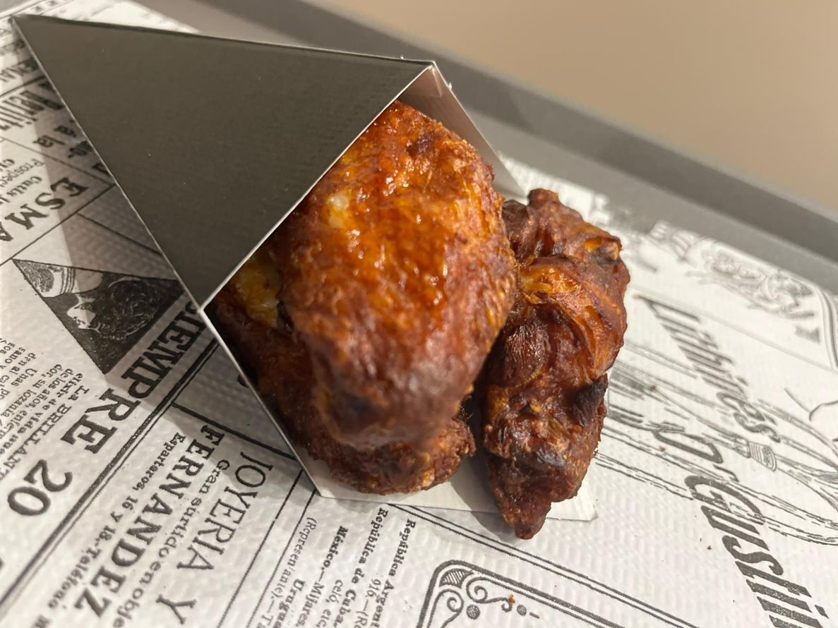 Due pezzi di pollo glassati in un cono di carta scura su un involucro alimentare stampato.