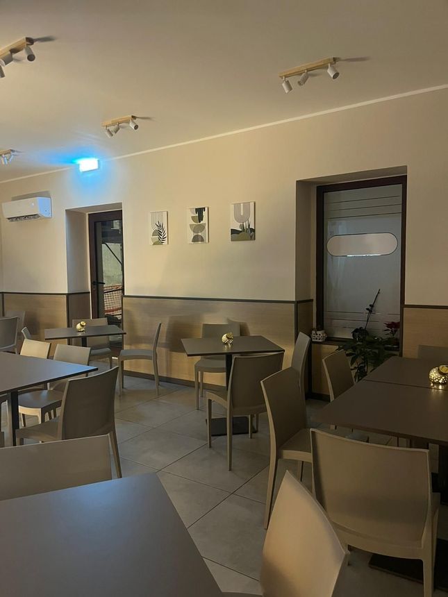 Interno vuoto di un caffè con tavoli e sedie, luci calde e una porta sul retro.
