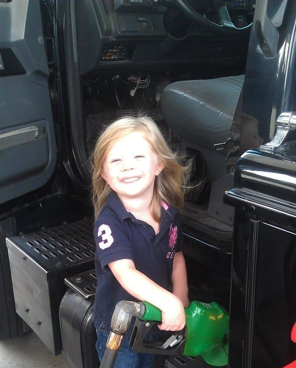 A little girl pumping gas into a truck with the number 3 on her shirt