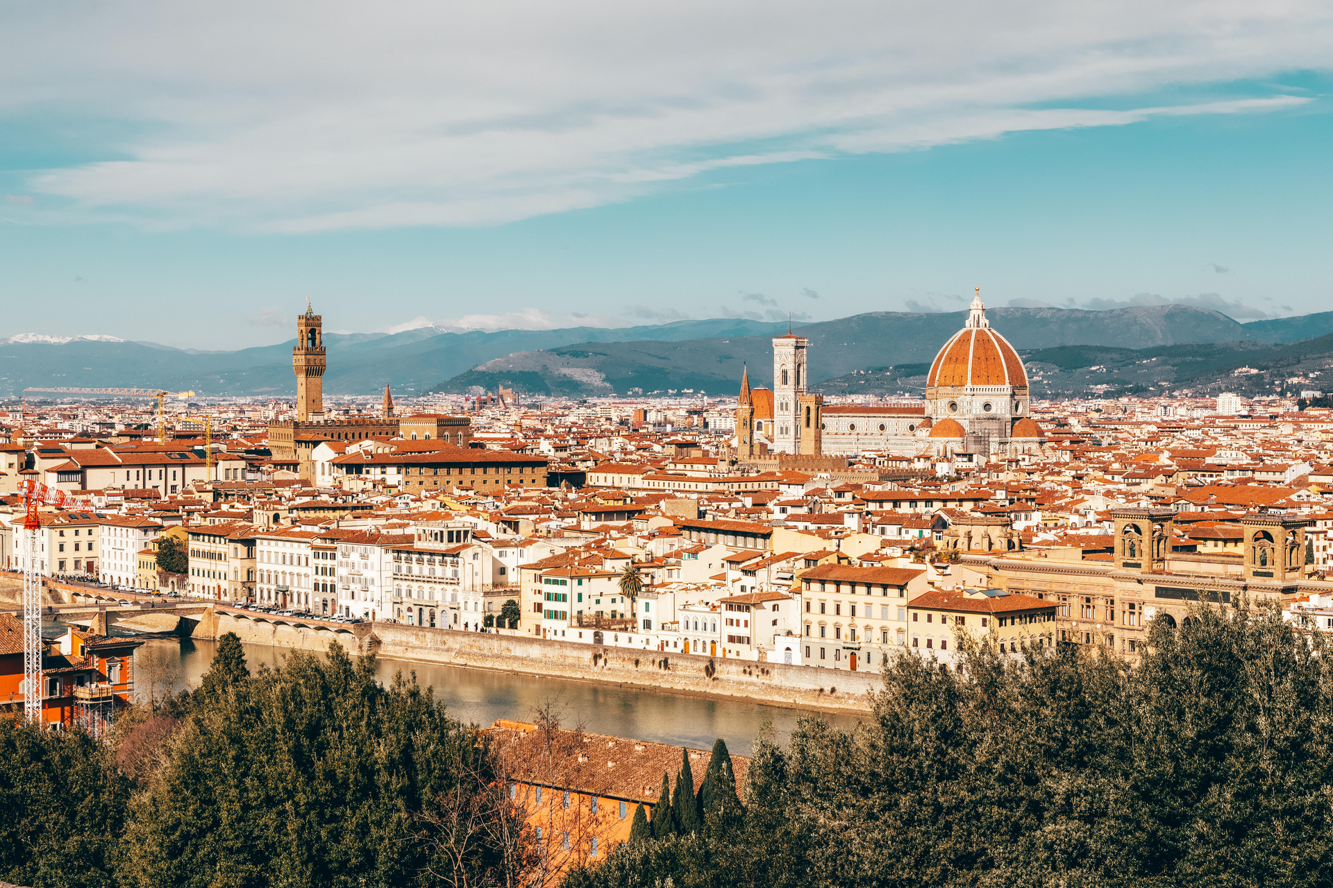 Cityscape of Florence, Italy with the Duomo dome prominent, terracotta rooftops, and a river.