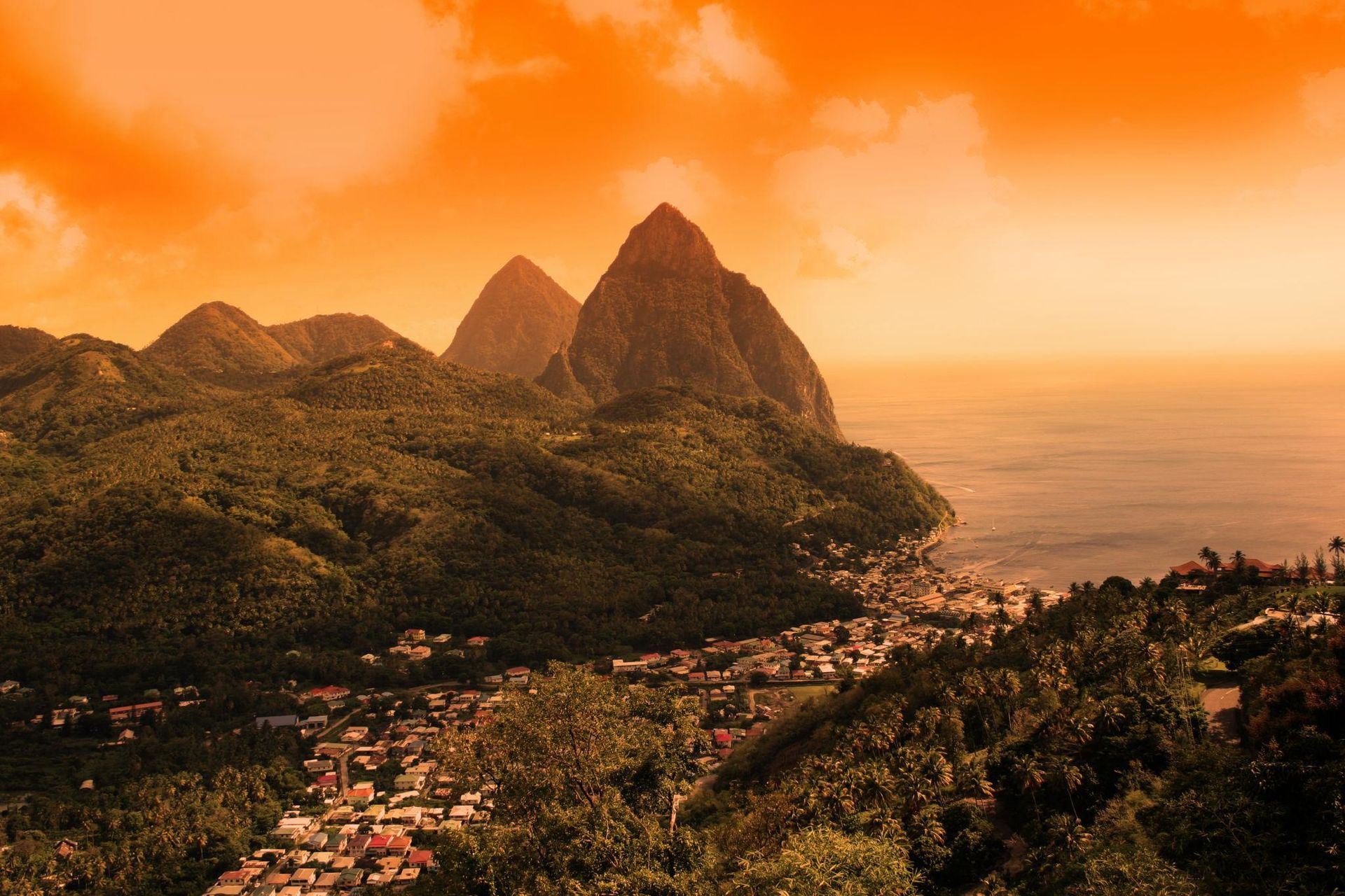Dramatic sunset over the Pitons, volcanic mountains in St. Lucia. Village at the base, ocean on the right.