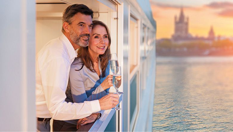 Couple on a boat enjoying champagne, overlooking a cityscape at sunset.
