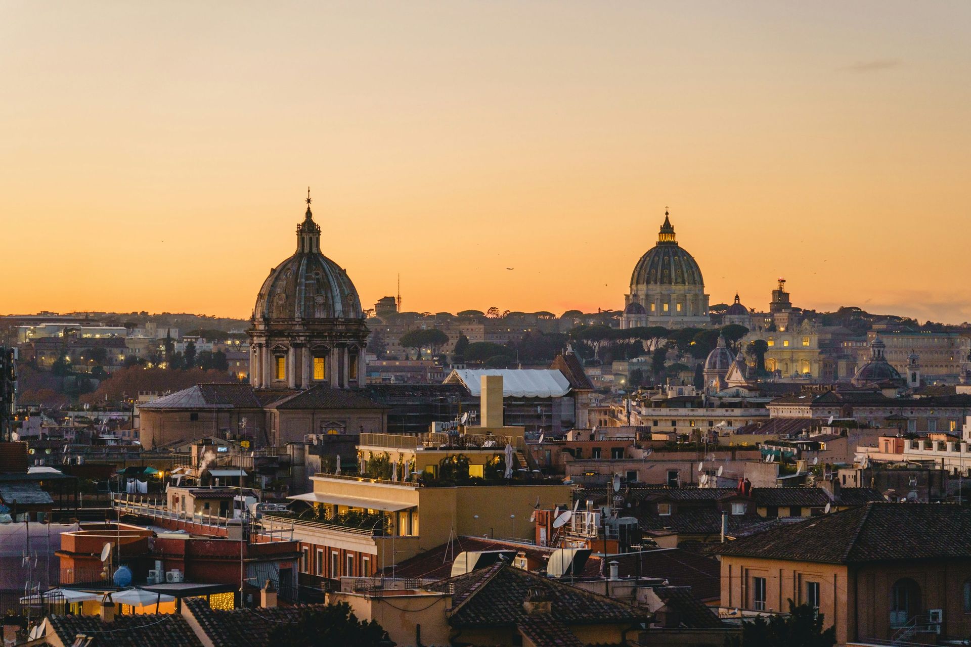Rome skyline featuring two prominent domes against a warm, orange-hued sunset sky.
