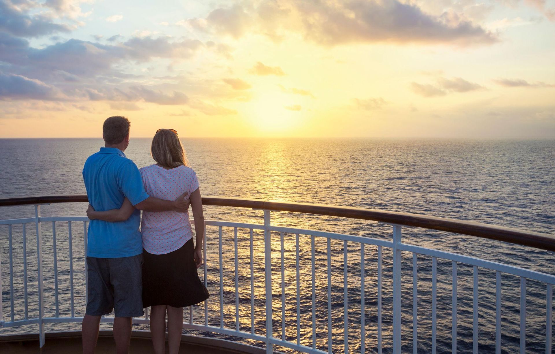 Couple on a ship deck looking at a sunset over the ocean.