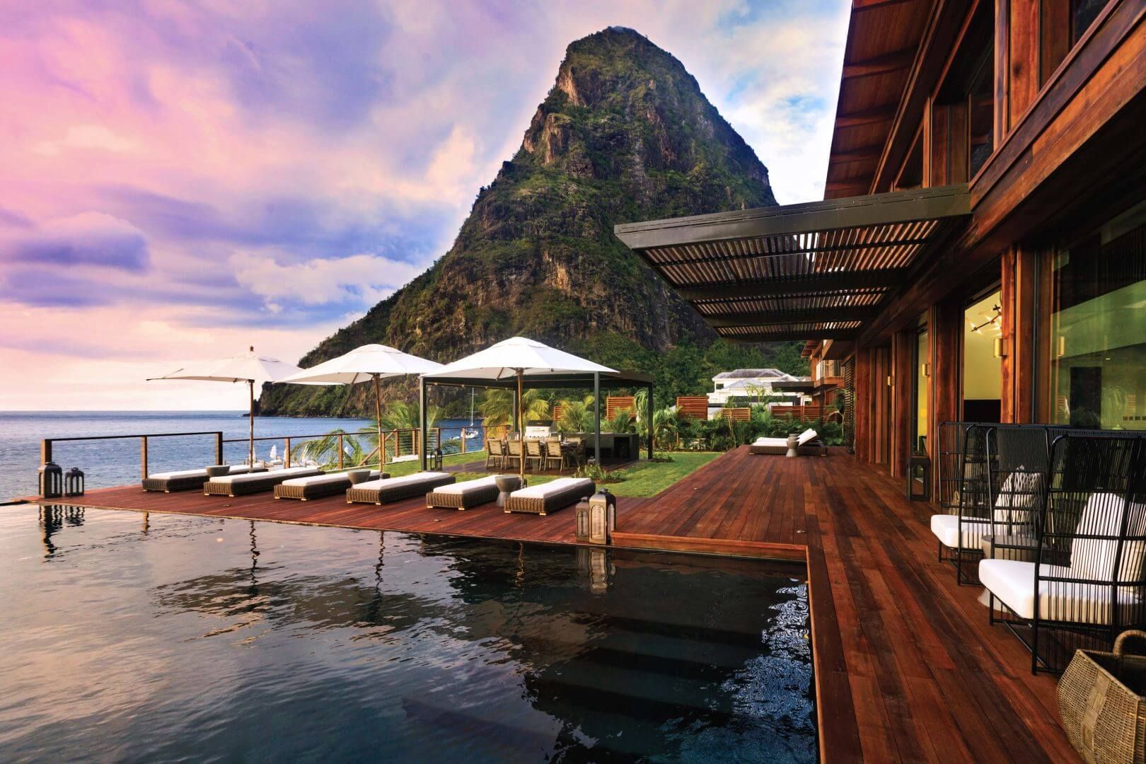 Poolside view of a luxury resort with the Pitons mountains in the background, blue sea, and wooden deck.