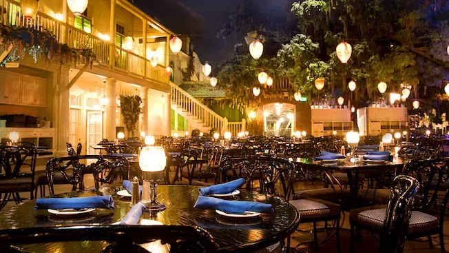 Outdoor restaurant at night, tables set for dining. Lanterns hang from trees and overhead.
