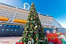 Christmas tree in front of a cruise ship. Presents are below the tree. The sky is blue.