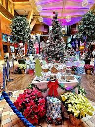 Christmas decorations: trees, gifts, poinsettias, and gingerbread houses in a brightly lit interior space.