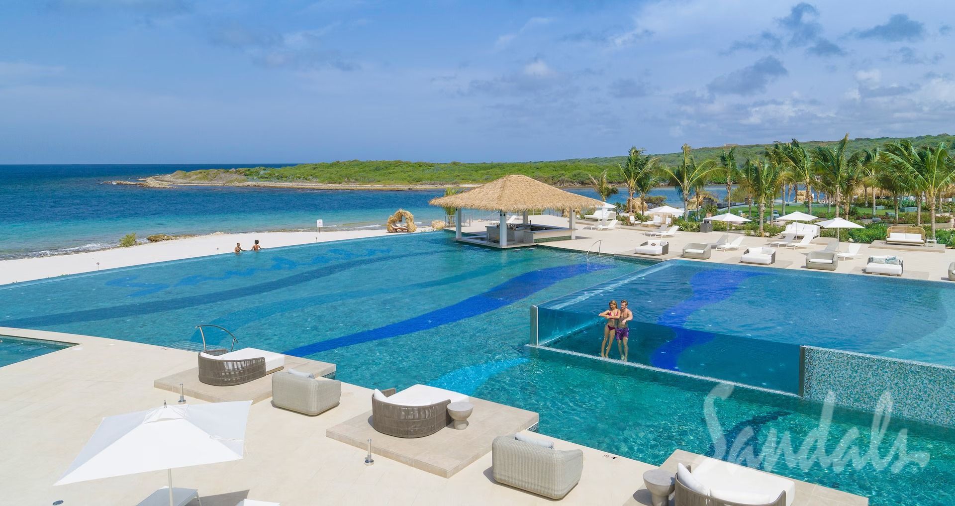 An aerial view of a luxurious resort pool with a swim-up bar, beach, and ocean.