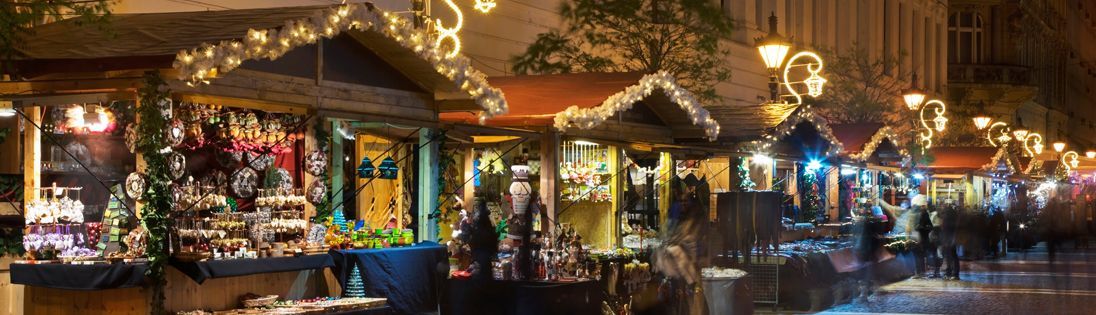 Christmas market stalls lit with garlands, set against a dark sky.