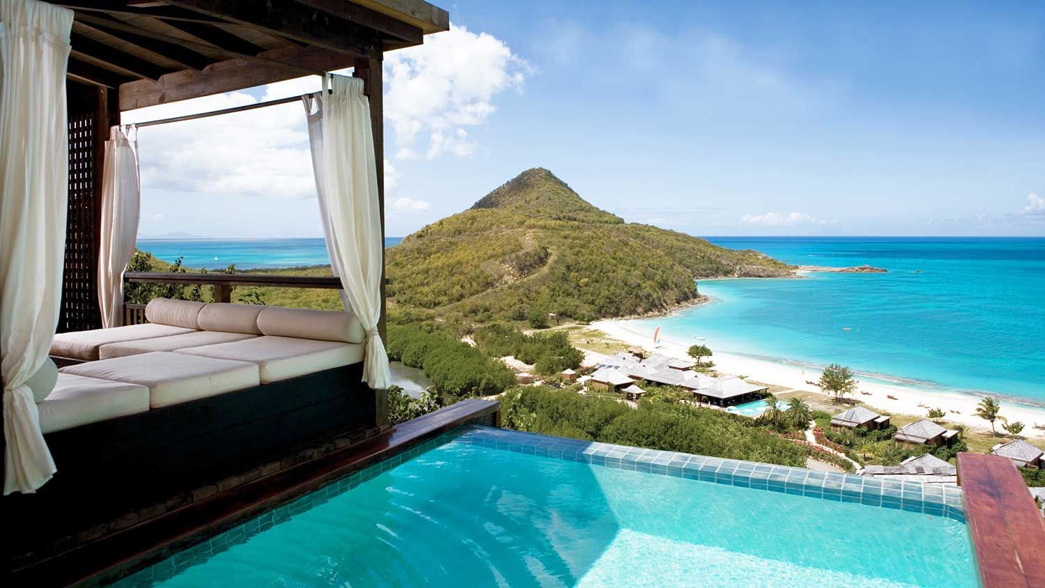 Pool with ocean view; gazebo with seating; beach and hill in background.