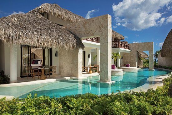 Luxury resort with private pools and thatched roof bungalows; turquoise water, blue sky.