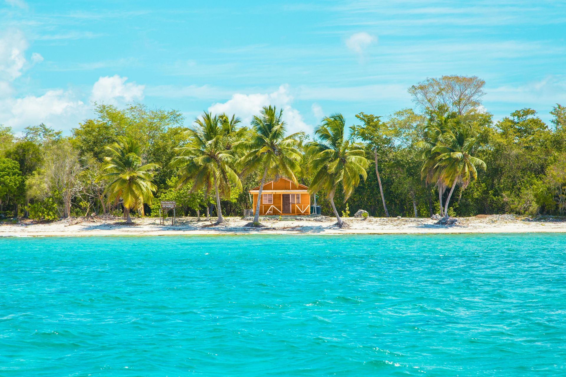 Tropical beach with turquoise water, sand, palm trees, and a small orange building.