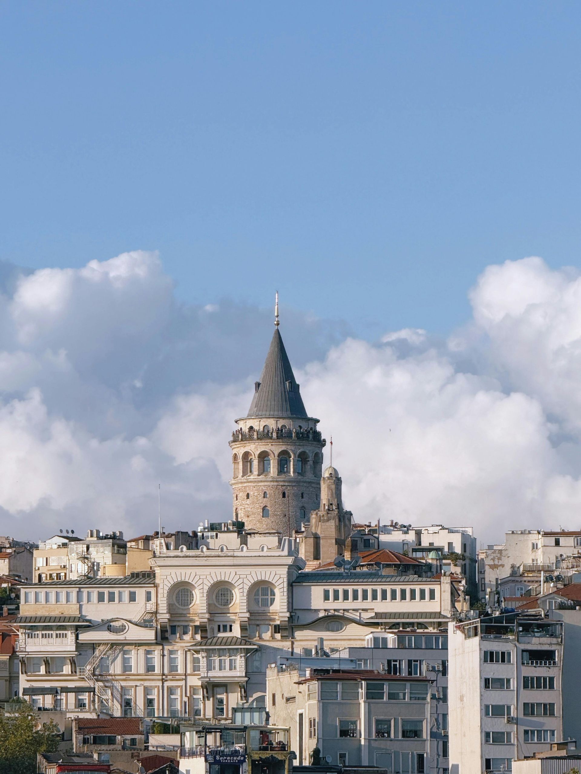 Galata Tower, Istanbul, Turkey, surrounded by buildings against a blue sky with puffy clouds.