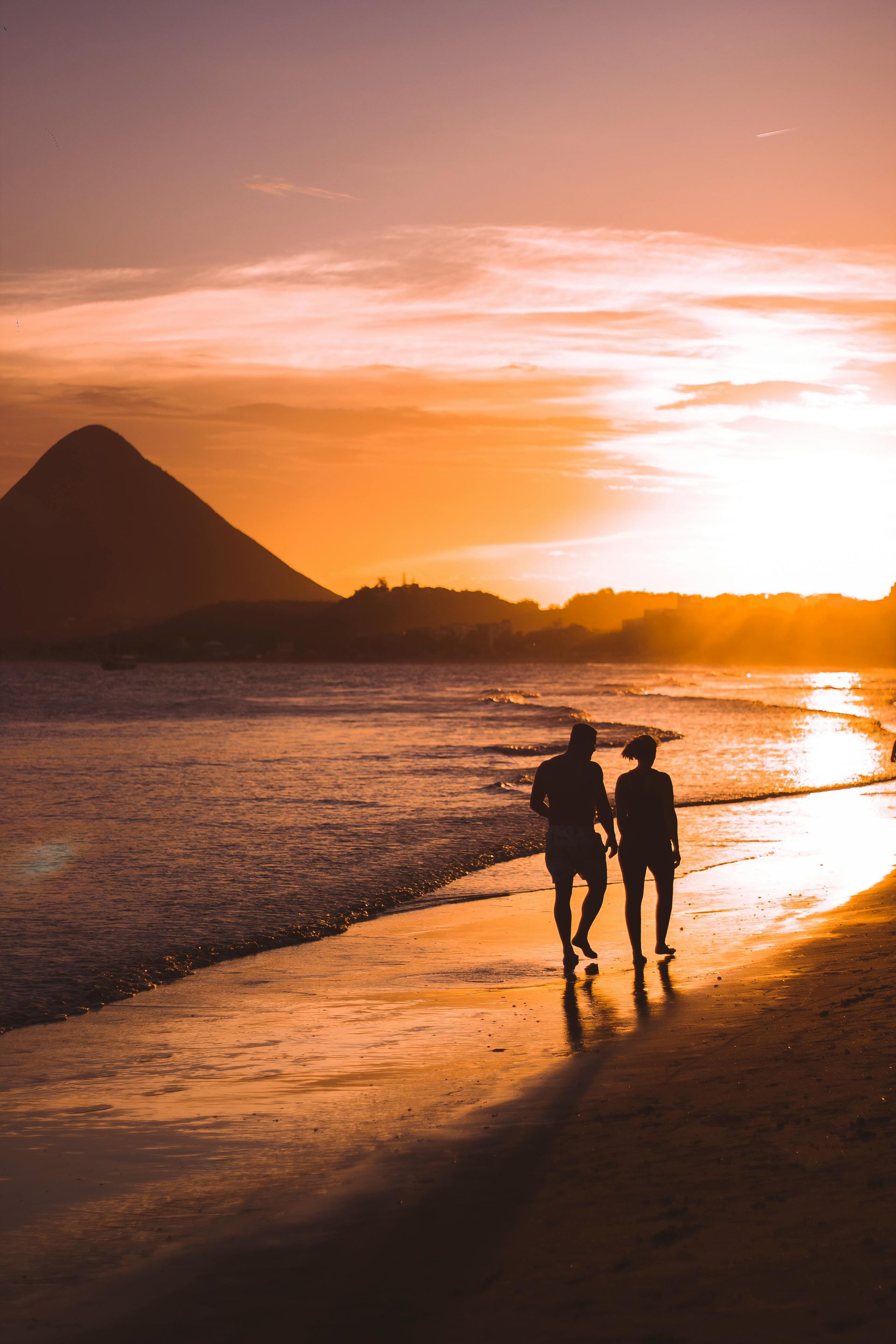 Couple walks along the beach at sunset; golden light, mountain silhouette.