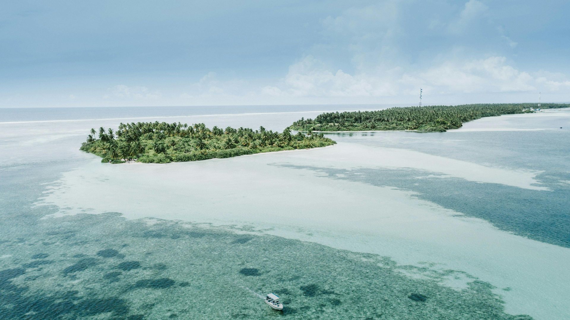 Islands with lush green trees surrounded by turquoise water under a light blue sky.