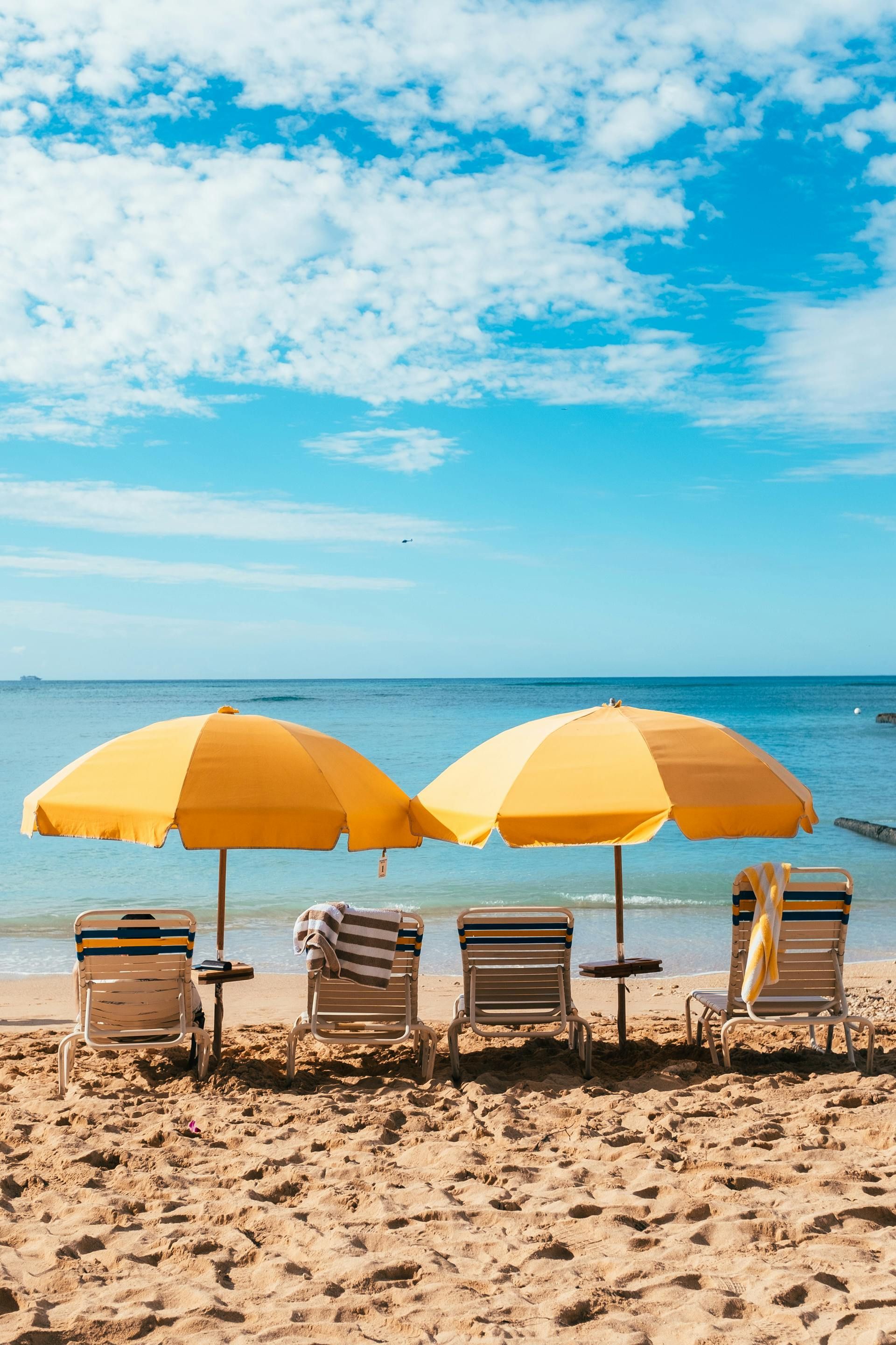 Beach scene with yellow umbrellas, chairs, and calm blue ocean under a bright sky.