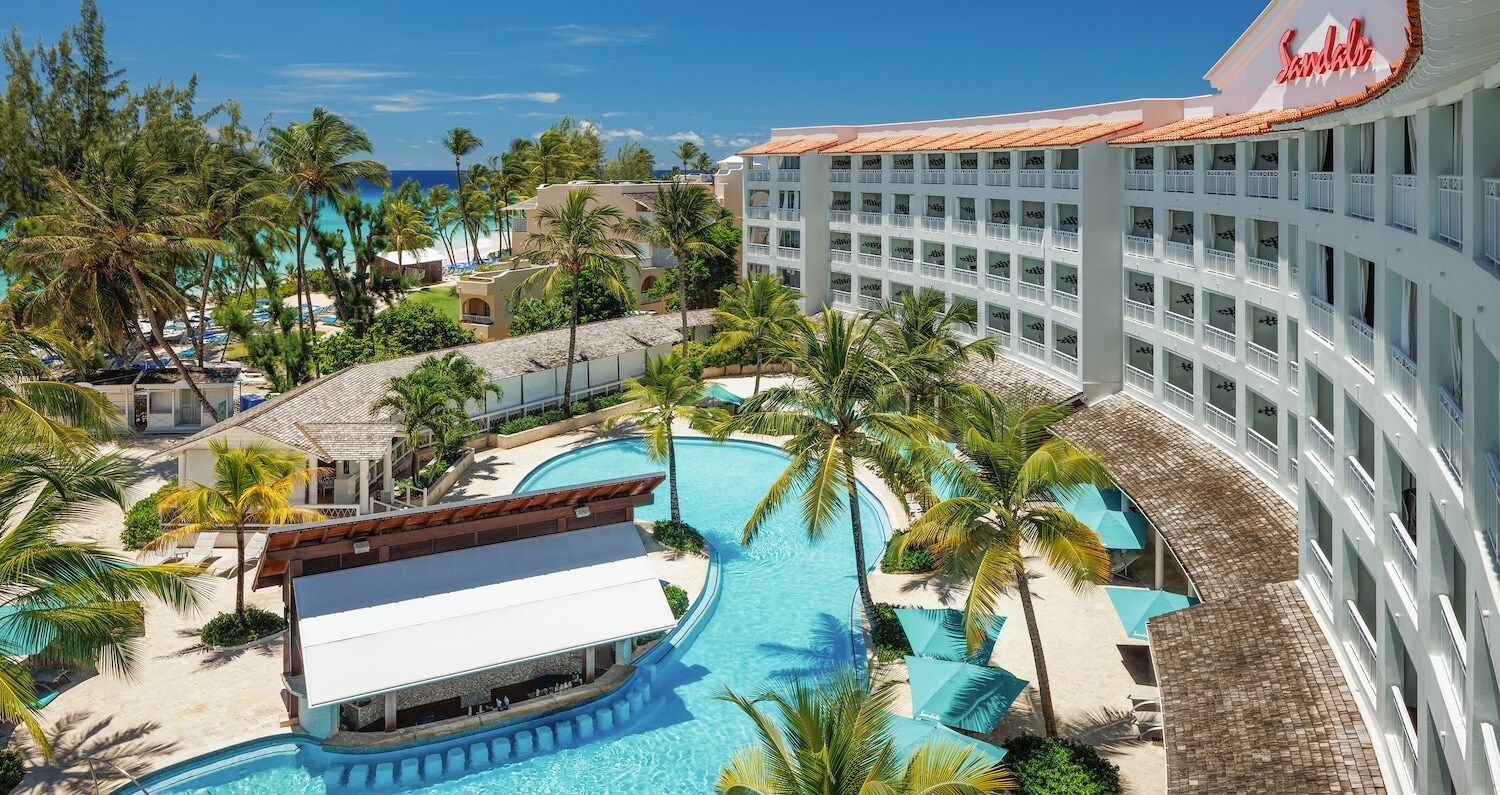 Pools and resort buildings at Sandals resort, with palm trees and ocean view in the background.