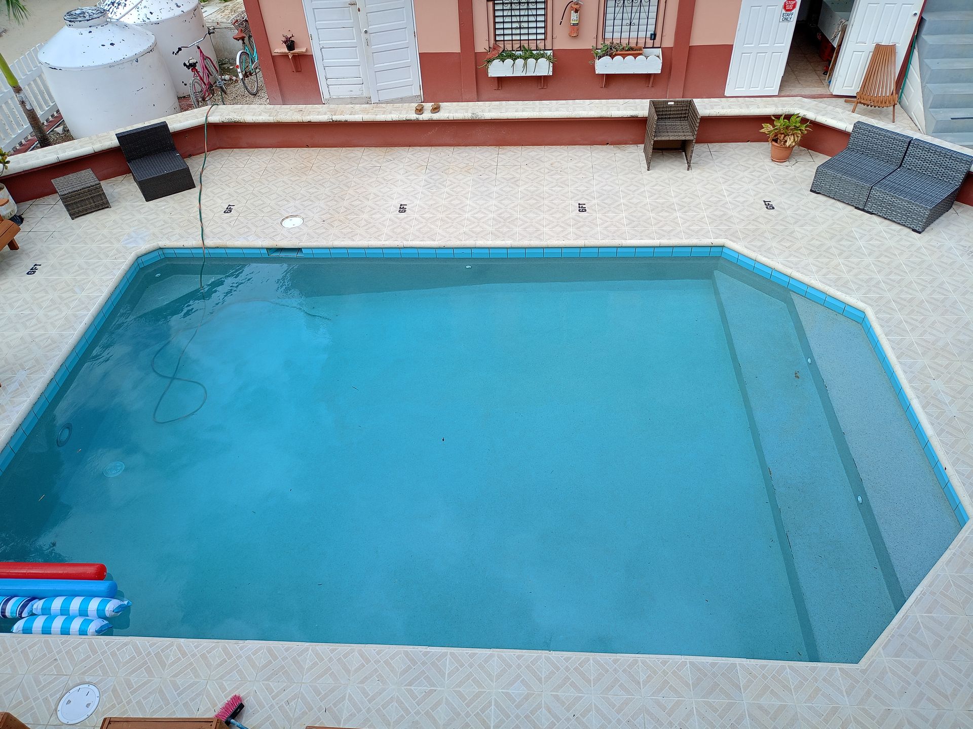 Blue swimming pool outside a building with chairs and white tanks.