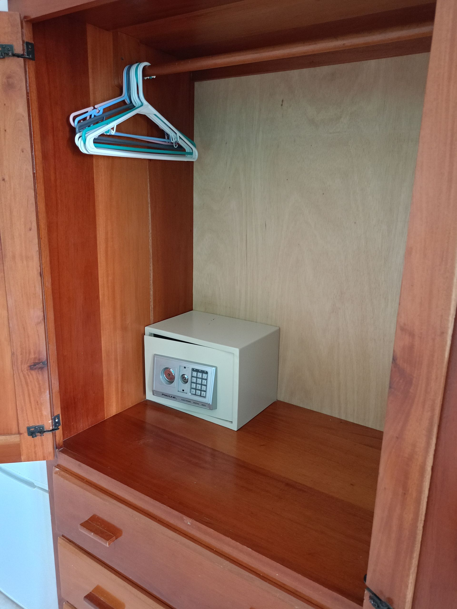 Wooden wardrobe with open doors. Contains a safe, hanger, and drawers.