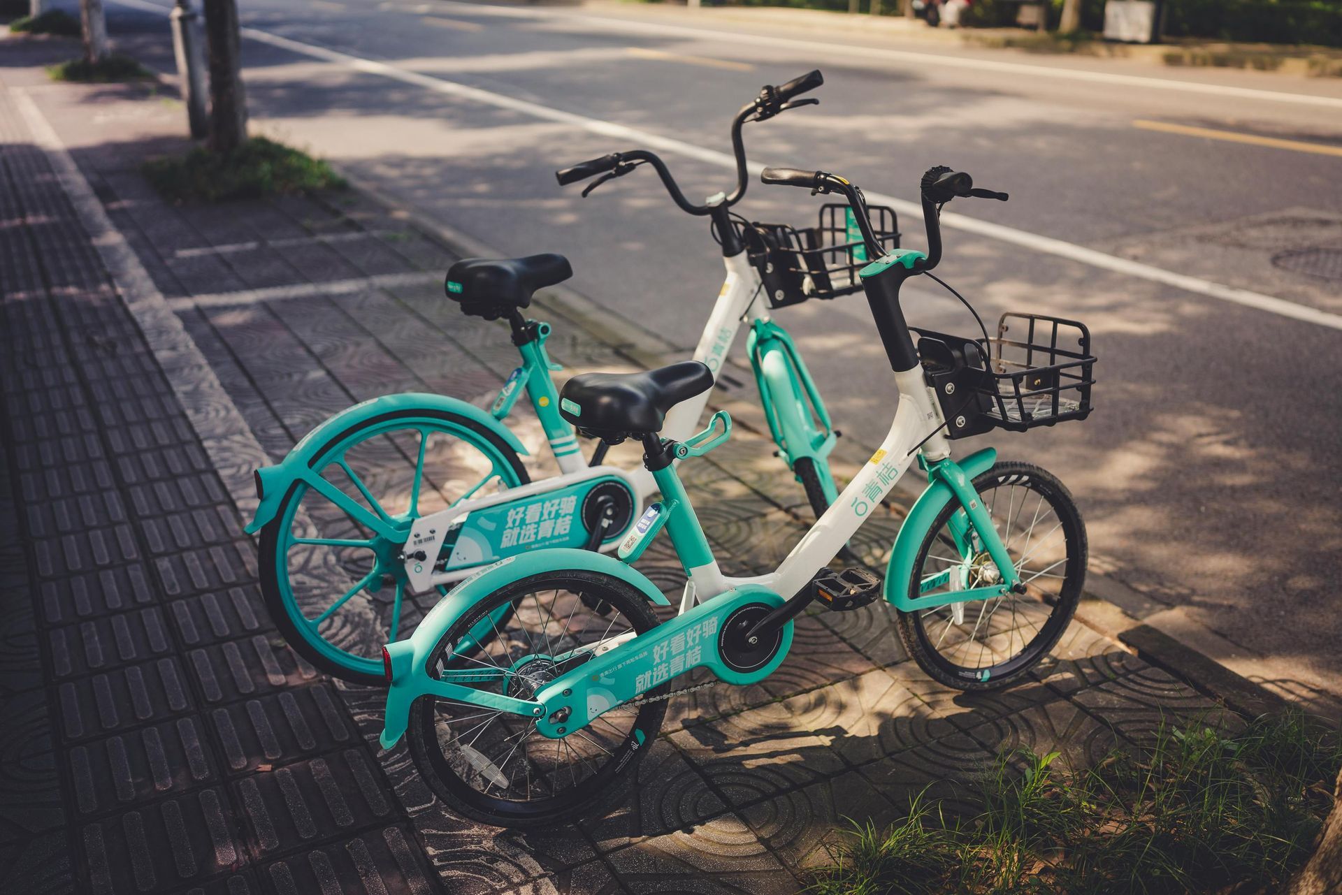 Two teal and white shared bicycles parked on a sidewalk next to a street.