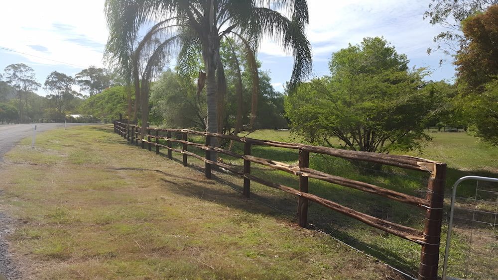 A Wooden Fence Surrounds A Grassy Field Next To A Road — D.T. Fencing In Bakers Creek, QLD