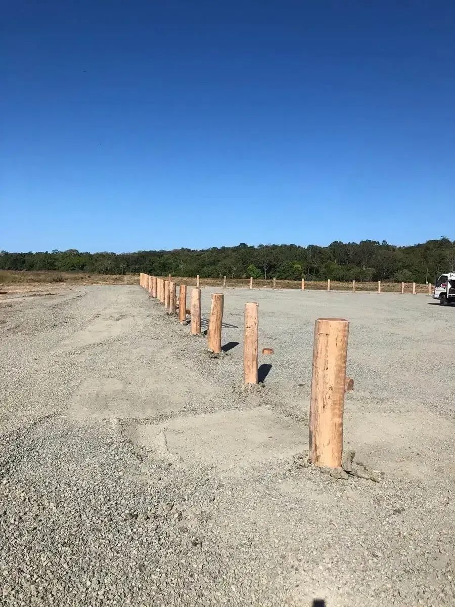 A row of wooden poles in a gravel parking lot. — D.T. Fencing In Bakers Creek, QLD