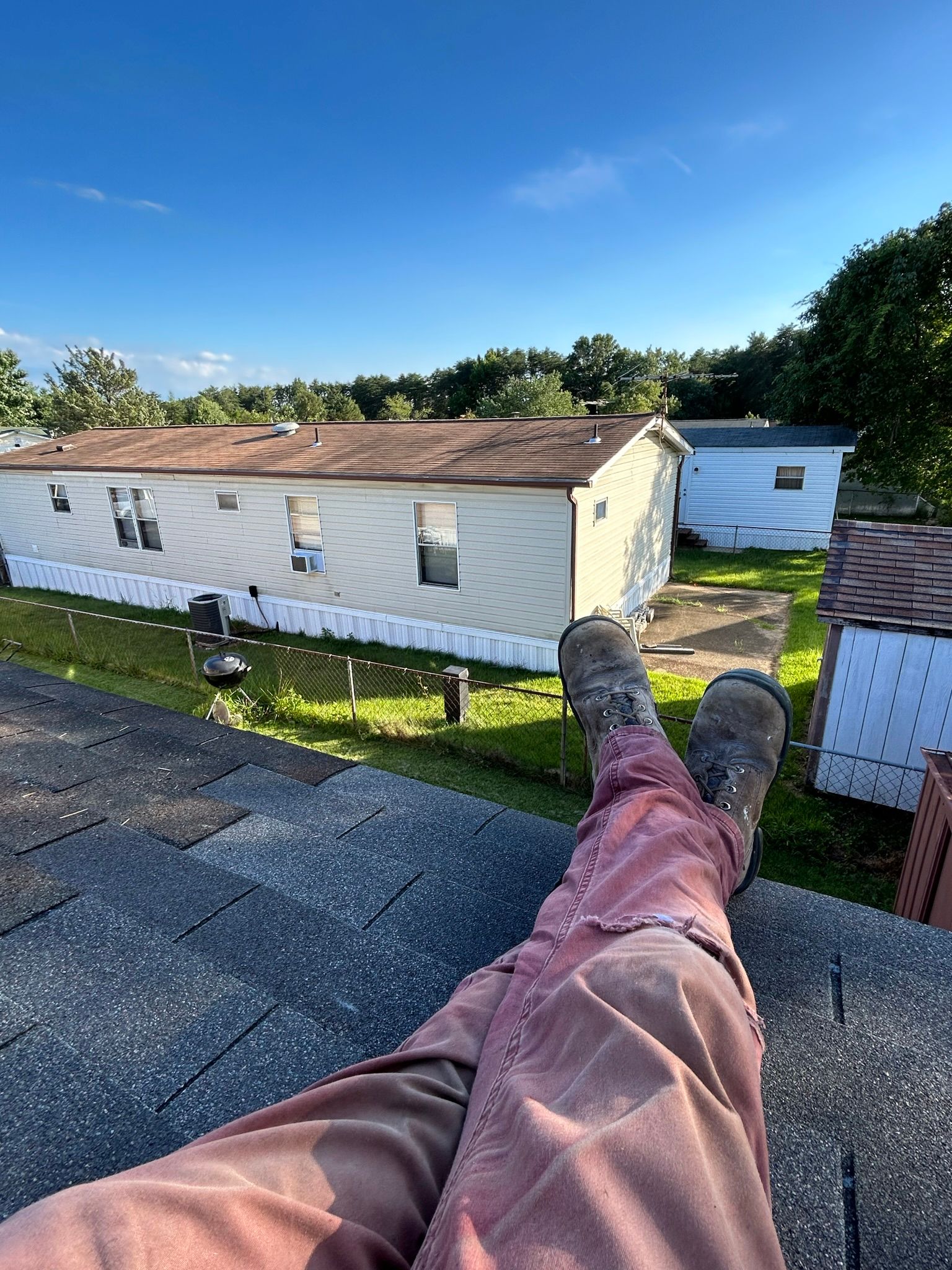 A person is laying on a roof with their feet up in front of a mobile home.