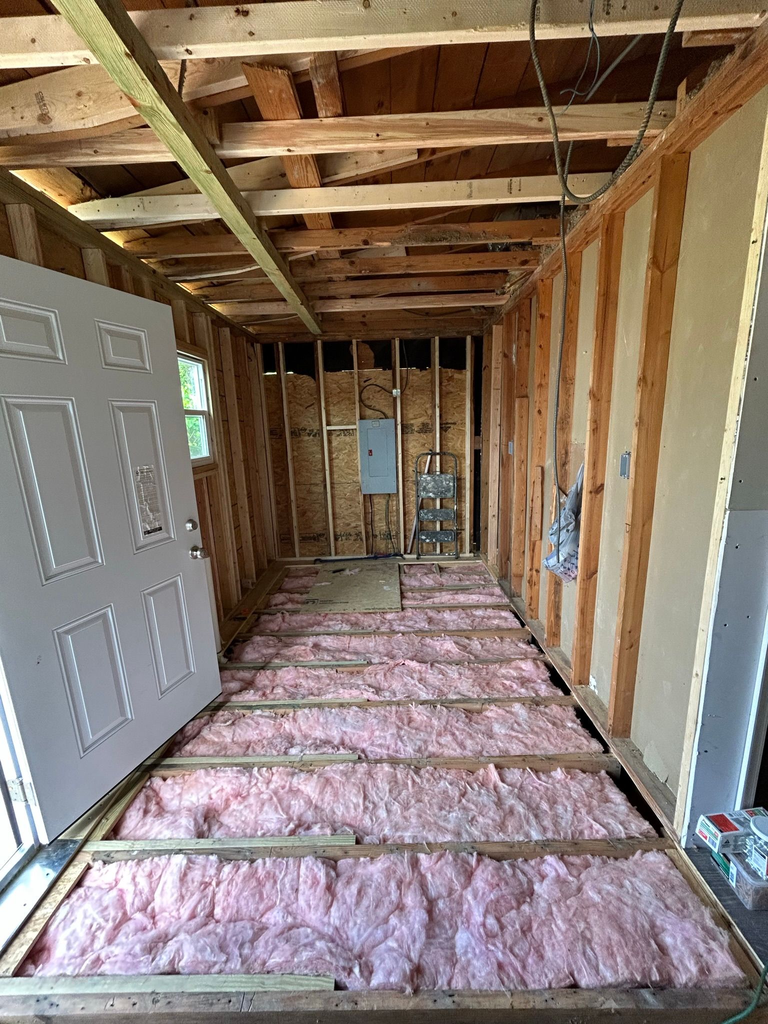 A room with a door open and pink insulation on the floor.