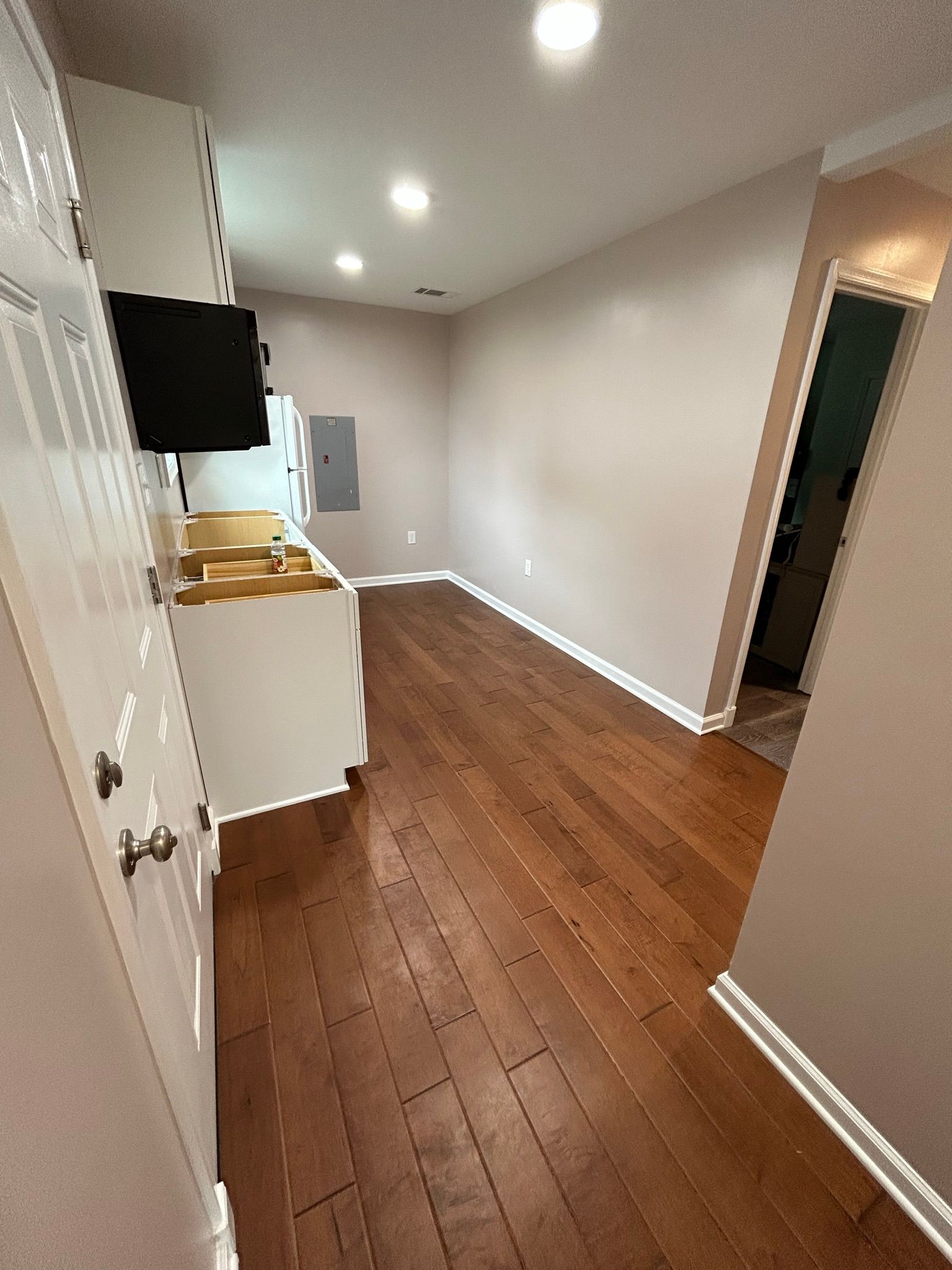 A long hallway leading to a kitchen with hardwood floors and white cabinets.