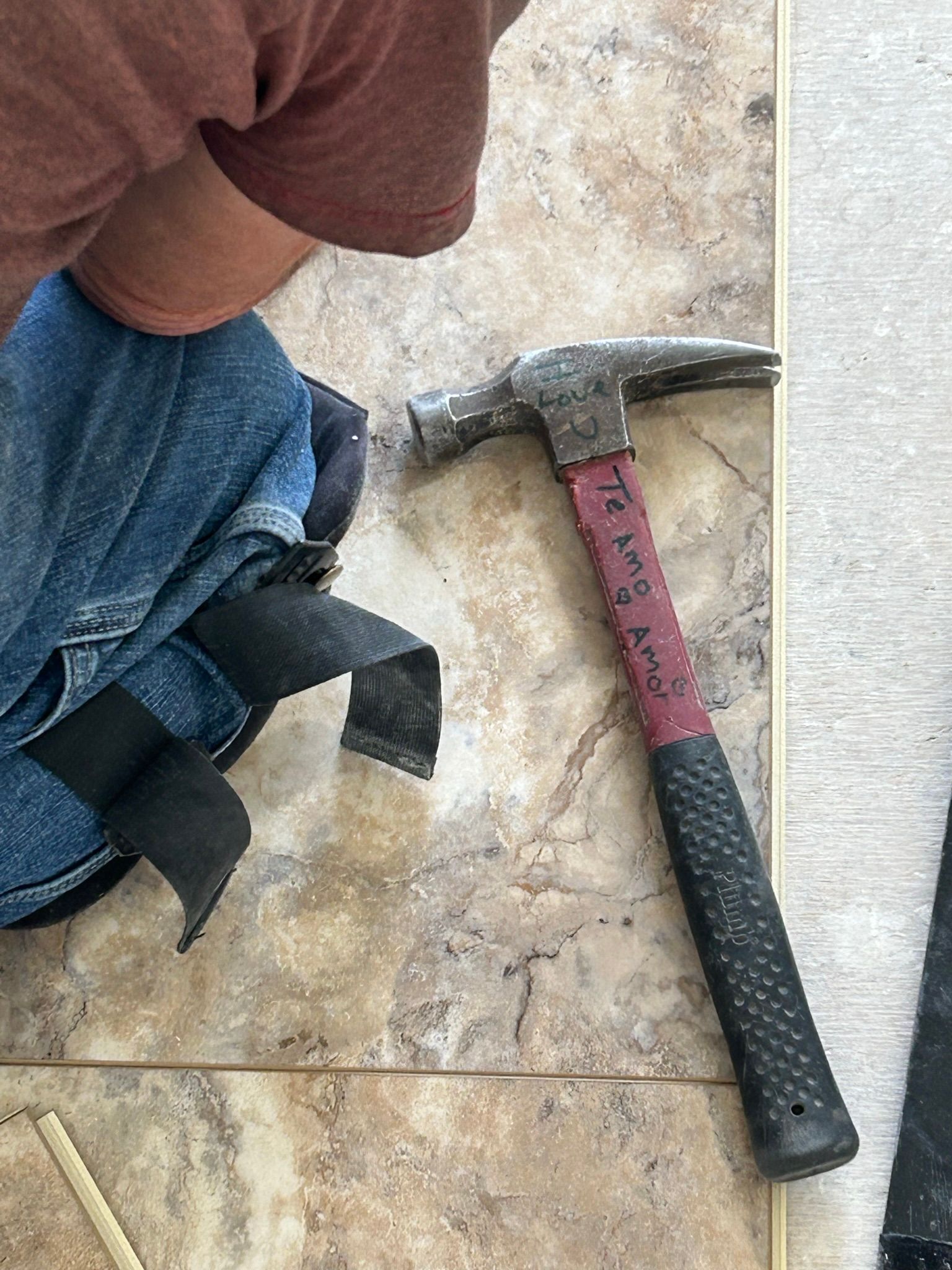 A person is kneeling down next to a hammer on the floor.