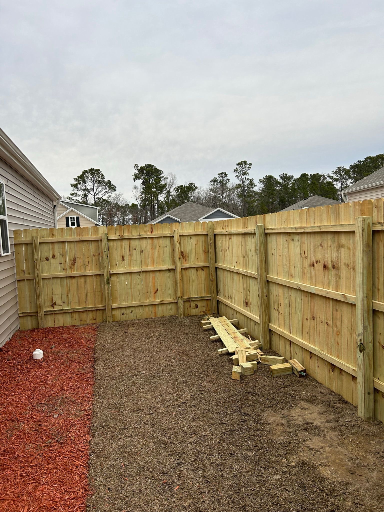A wooden fence is in the backyard of a house.
