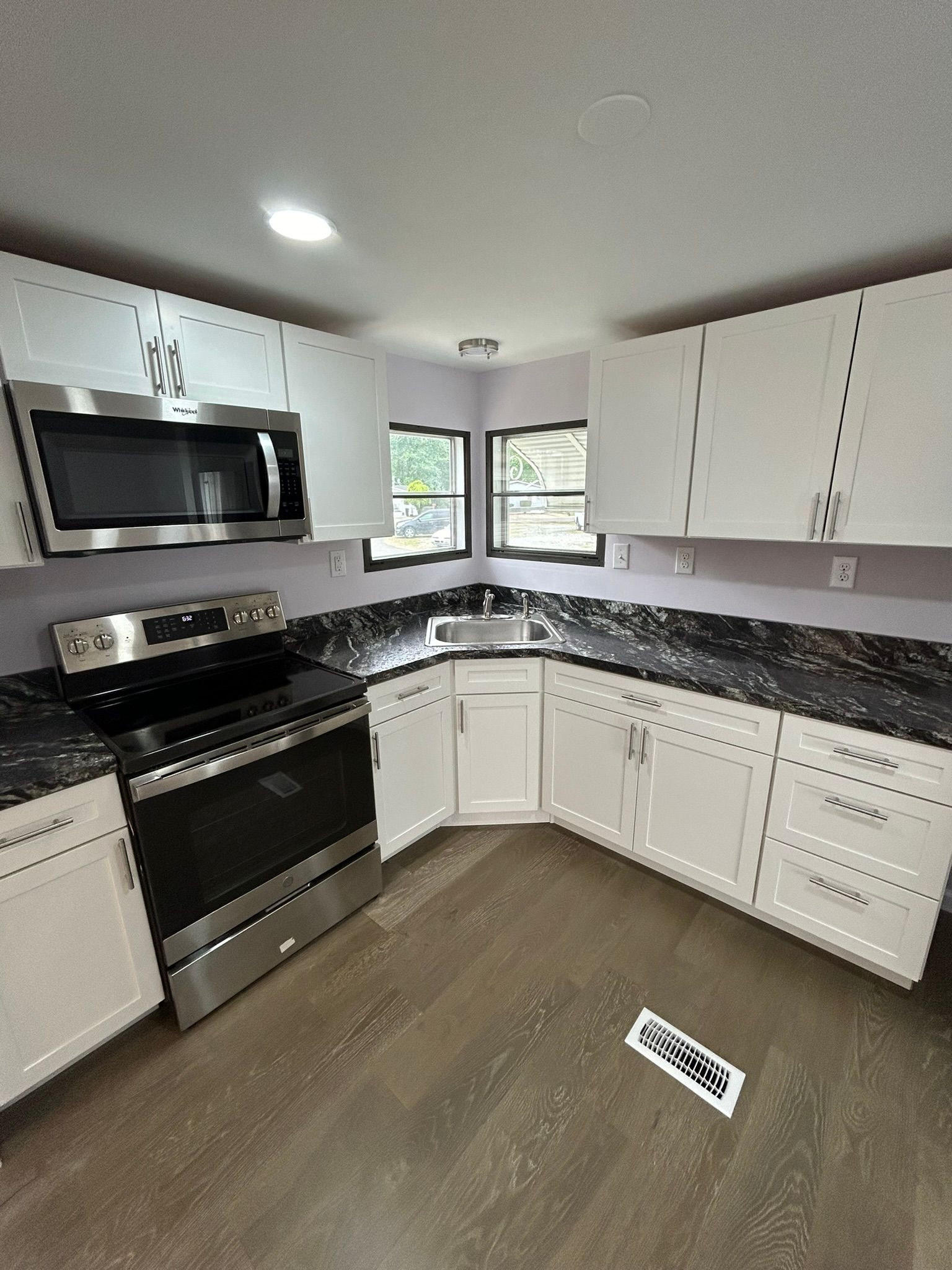 A kitchen with white cabinets , stainless steel appliances , and granite counter tops.