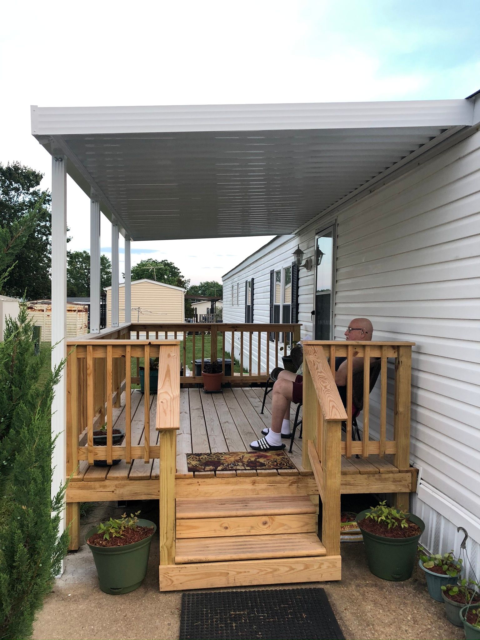 A man is sitting on a porch of a mobile home.