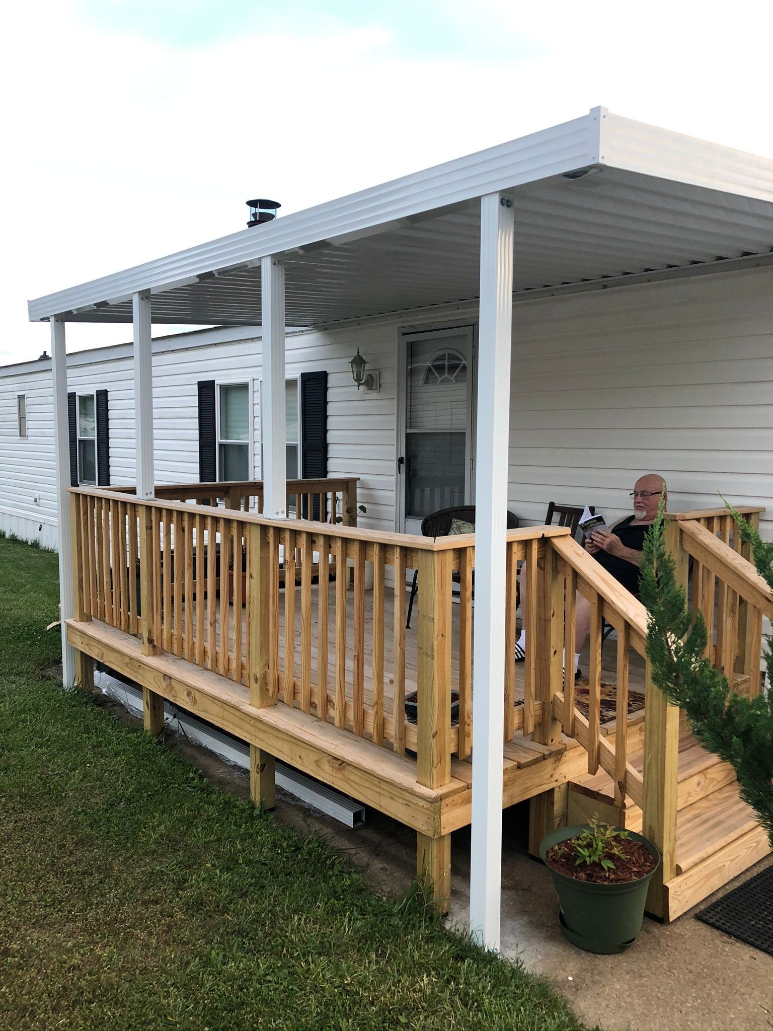 A man is sitting on a porch of a mobile home.