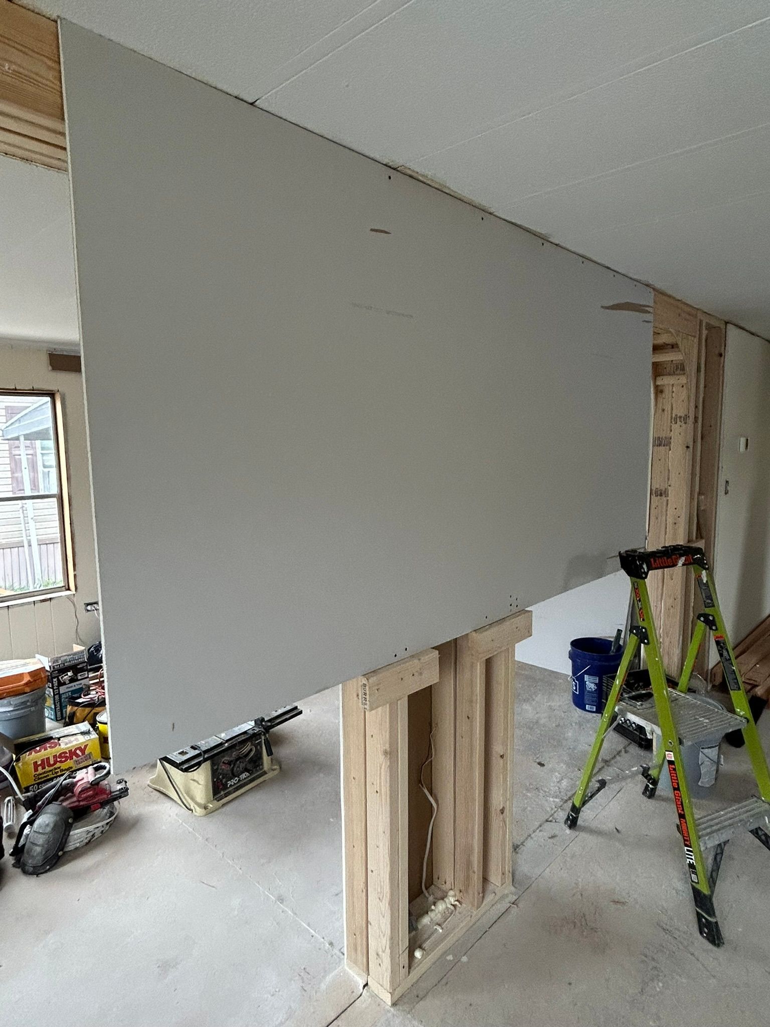 A room is being remodeled with a large piece of drywall hanging from the ceiling.