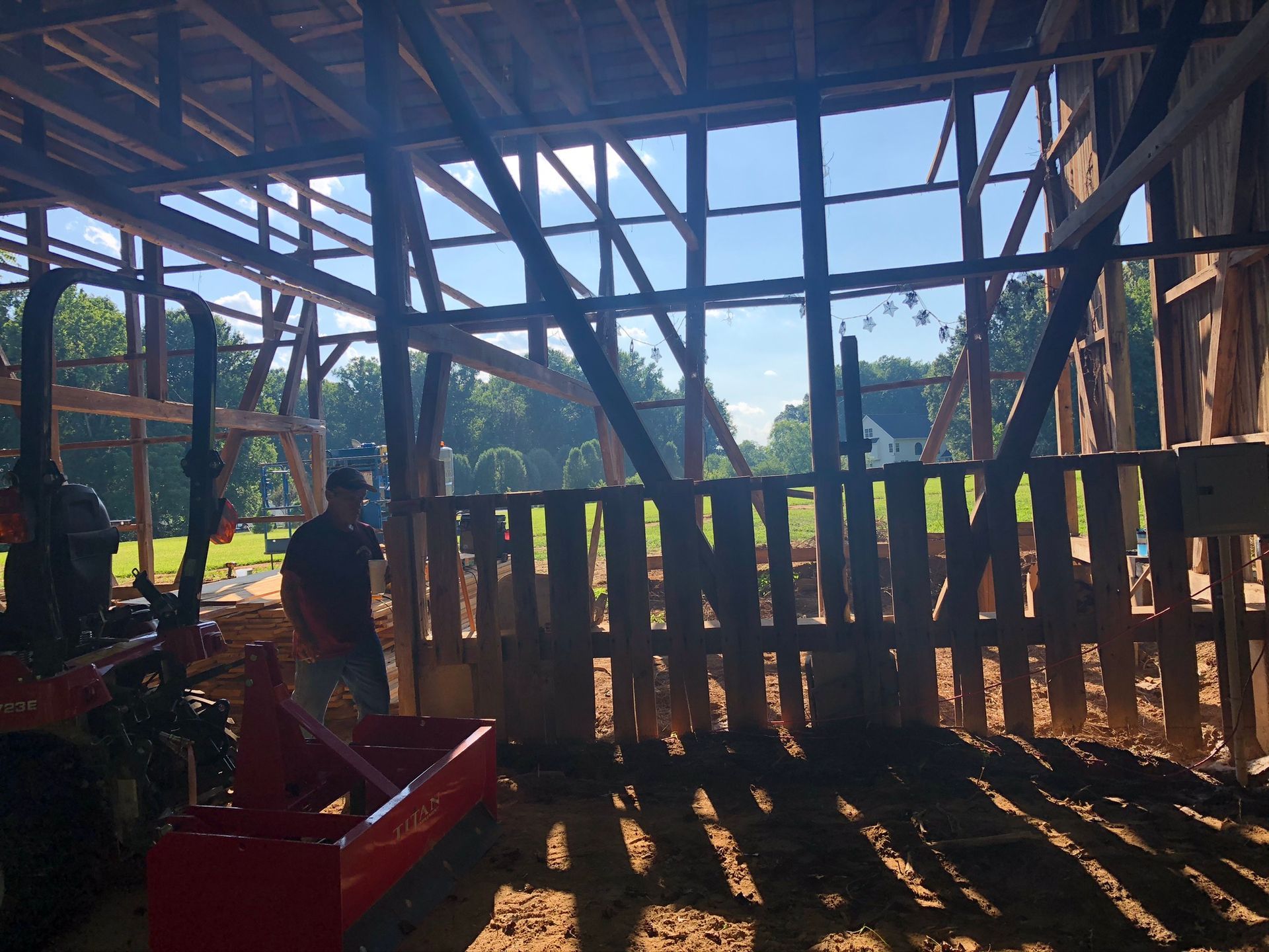 A man is standing inside of a barn with a tractor in the background
