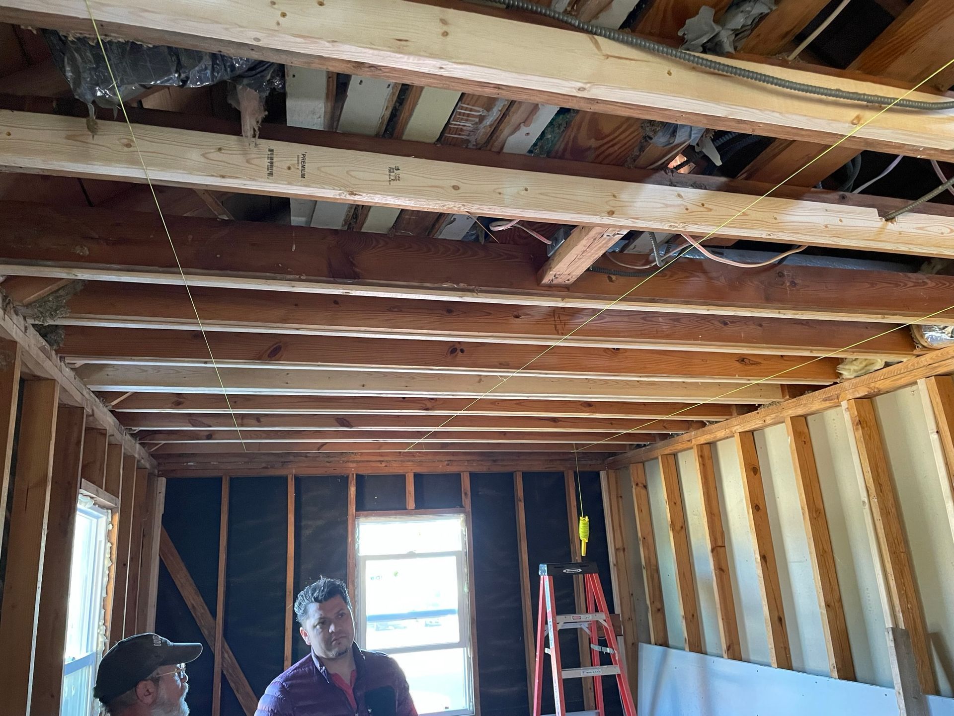 Two men are standing in a room under construction with a ladder.