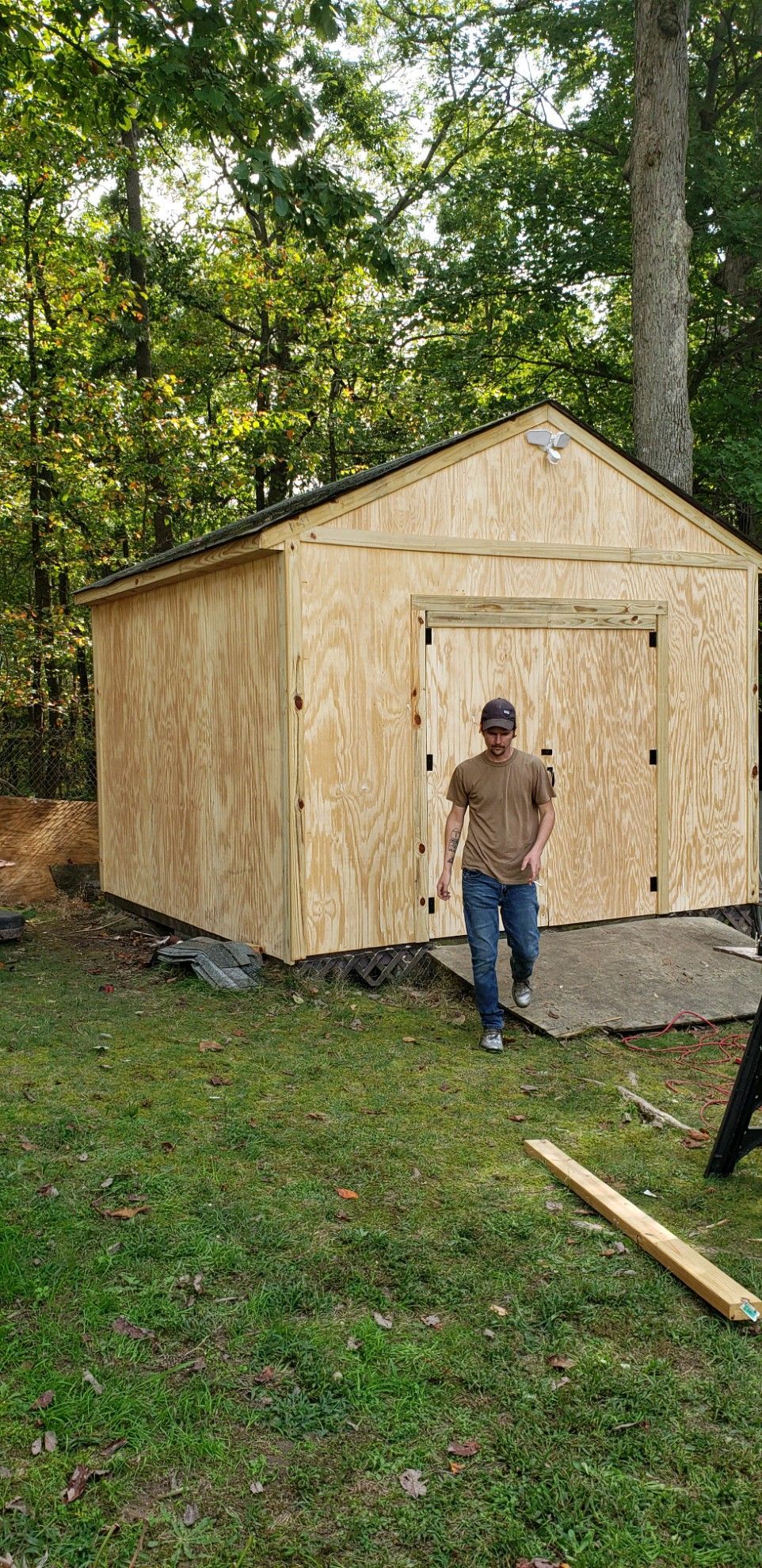 A man is standing in front of a wooden shed in a backyard.