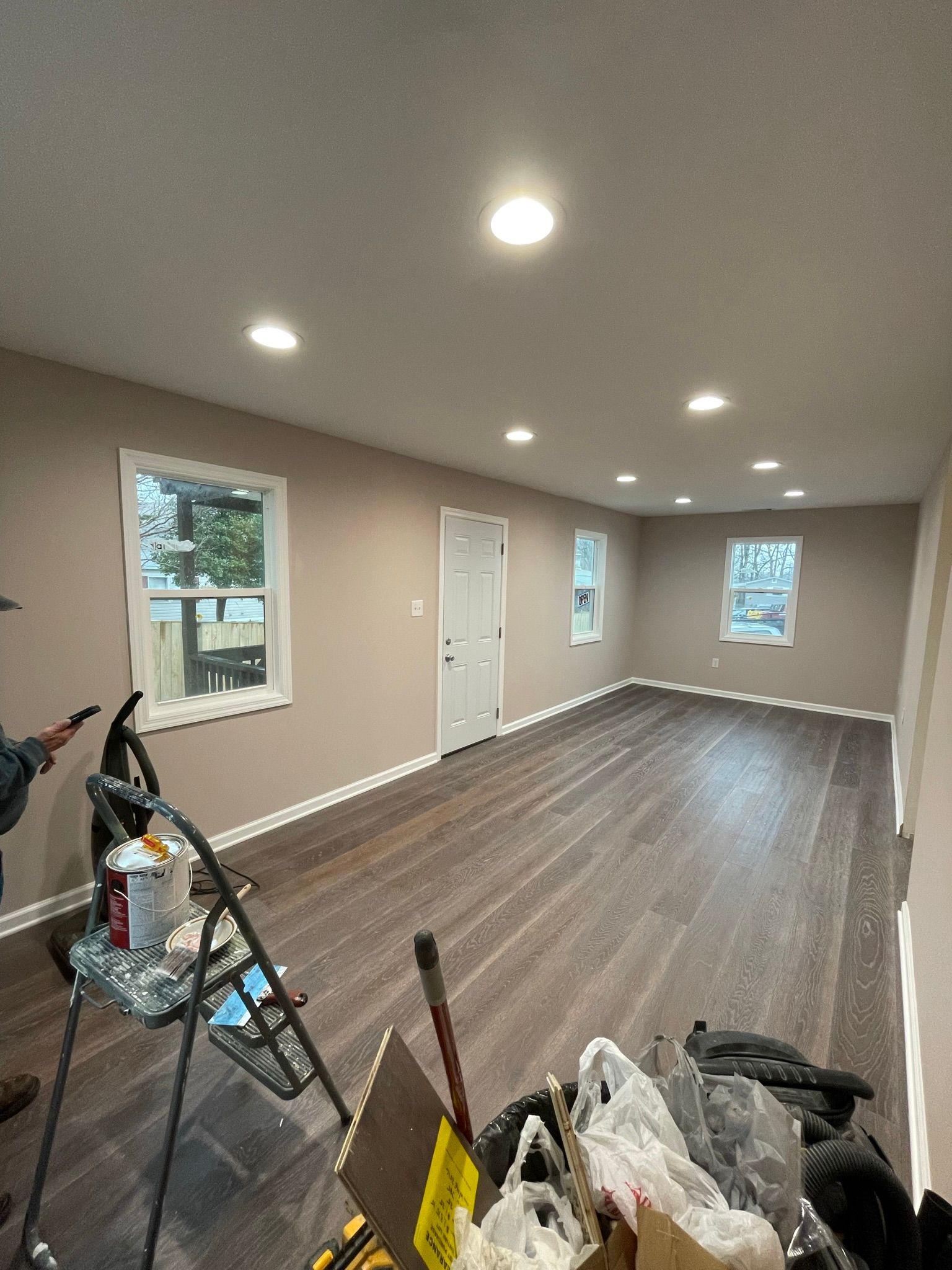 A man is painting a wall in a large room with hardwood floors.